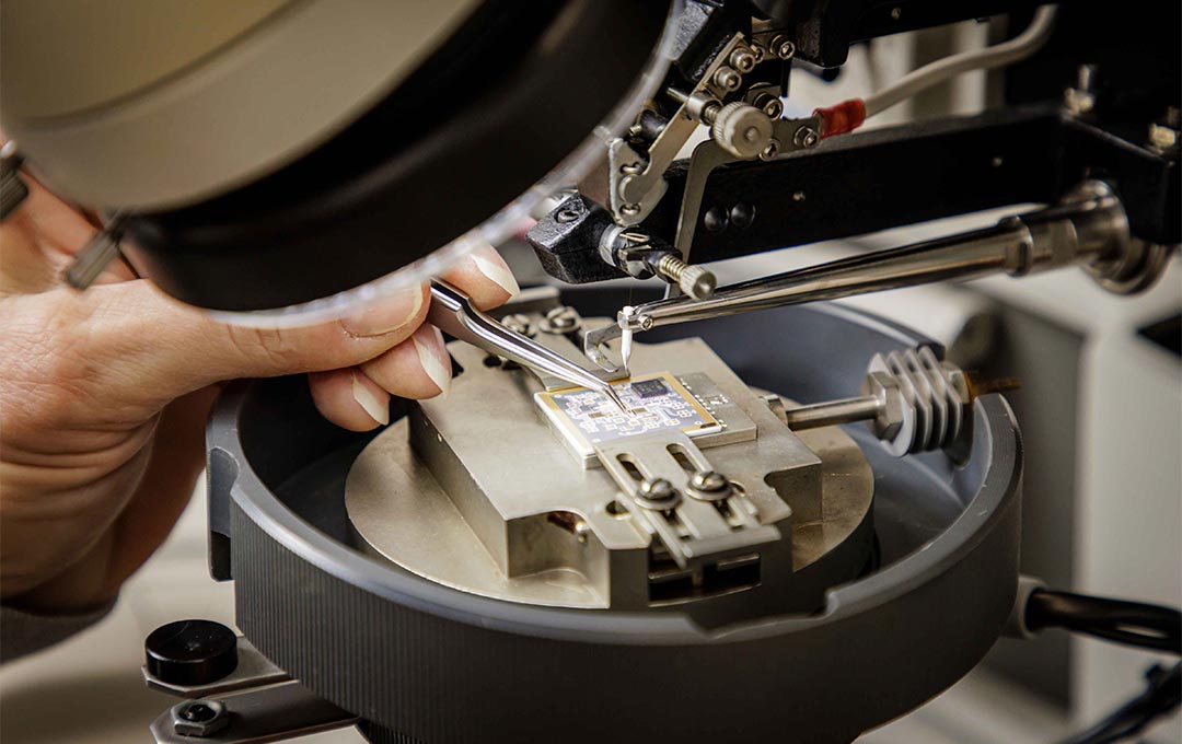 Microchip under a microscope with someone using a pair of tweezers to analyze the chip.
